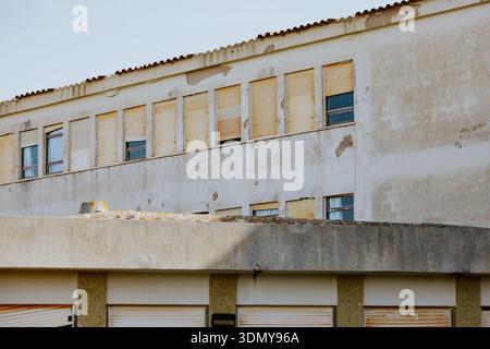An old, weathered building displays a worn facade with peeling paint and closed shutters. The image captures the aged texture and architectural detail Stock Photo