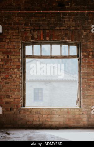Sunlight streams through a rustic window in an old brick building, casting a warm glow on the textured walls. The scene outside appears blurred, creat Stock Photo