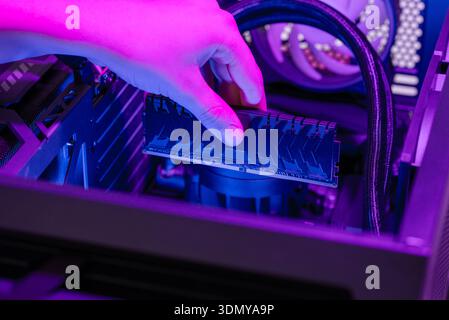 Installing RAM memory module into motherboard inside gaming computer, rgb lighting highlighting hardware upgrade, system assembly, performance computi Stock Photo