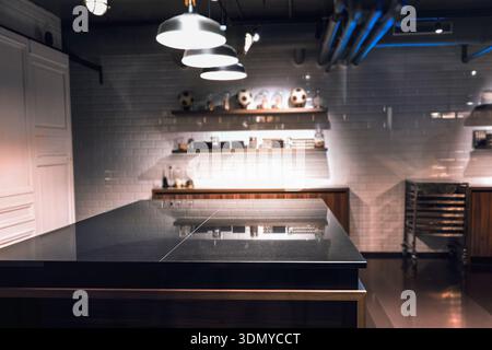 Sleek kitchen space showcases dark island countertop and industrial lighting against white tiled wall, kitchen interior Stock Photo