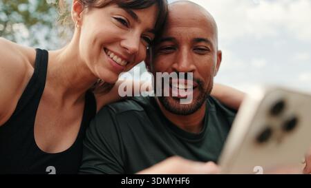 Close-up of athletic couple in love relaxing and using smartphone, focus on persons Stock Photo
