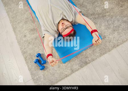 Overweight man stretching resistance band during home workout on mat, top view Stock Photo