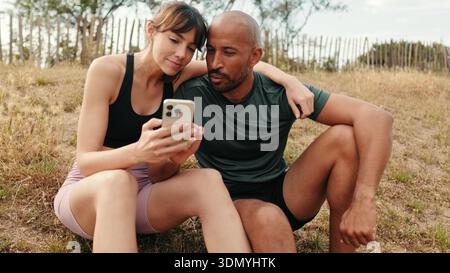 Close-up of athletic couple in love relaxing and using smartphone, focus on persons Stock Photo