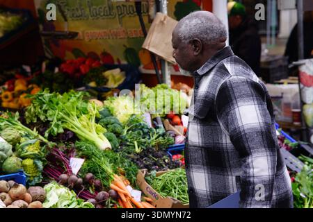 Elderly shopper examining fresh vegetables at a colourful market stall in Cambridge. Cambridge,England Stock Photo
