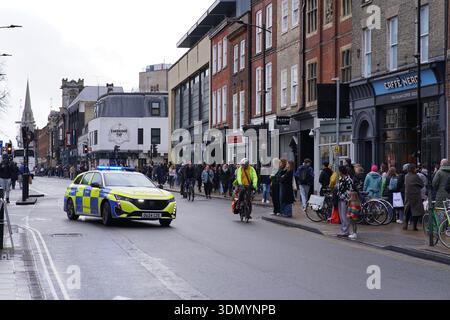 Police car patrolling a busy wet street in Cambridge city centre with pedestrians and cyclists. Cambridge,England Stock Photo