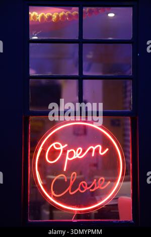 Red neon "Open Close" sign glowing in shop window at night.Cambridge,England Stock Photo