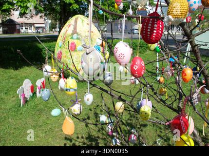 Festive Easter decorations with colorful handmade easter eggs hanging on tree branches in a city park. Handcrafted, painted, crocheted, and pattern. Stock Photo