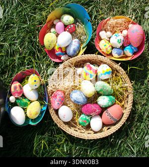 Top view of colorful hand painted Easter eggs arranged in wicker basket and decorative bowls on fresh green grass. Bright and pastel colors. Stock Photo