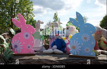 Pastel colored Easter bunny outdoor decorations, plush rabbit toys in a rustic spring garden setting. Pink, white folk Easter decoration copy space. Stock Photo