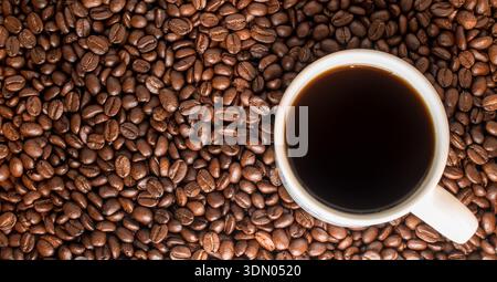 A white ceramic cup filled with black coffee surrounded by roasted coffee beans on a pale blue surface. Stock Photo