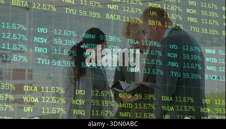 Reviewing papers, three colleagues wearing suits at glass wall in modern office with ticker overlay Stock Photo