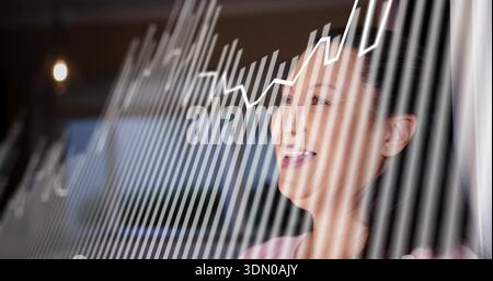 Smiling woman in pink top viewing data in office through striped glass with line-graph, copy space Stock Photo