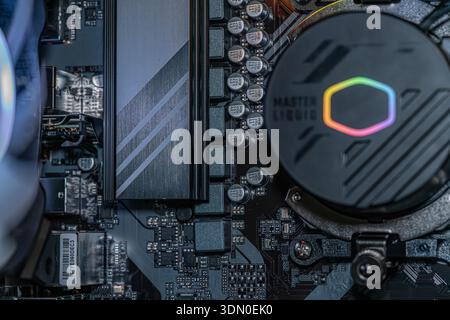 Gaming computer motherboard with RGB liquid cooling pump capacitors and semiconductor PCB circuitry inside desktop hardware system Stock Photo