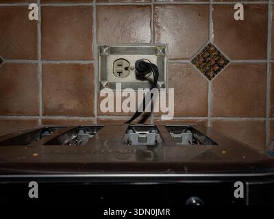 Toaster with power cord plugged into a wall outlet against brown tiled backsplash, captured in warm indoor lighting with household realism. Stock Photo