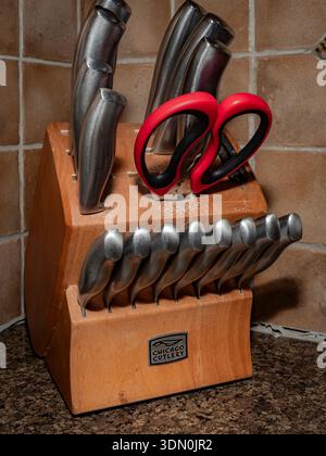 Chicago Cutlery knife block set with stainless steel knives and red-handled kitchen shears on granite countertop against tiled backsplash. Stock Photo