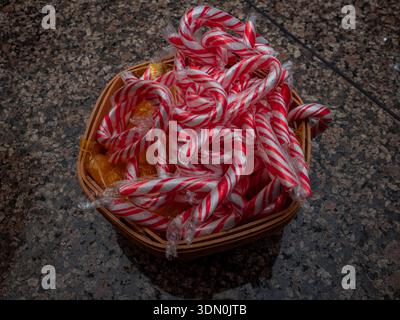 Basket filled with red and white peppermint candy canes and wrapped yellow sweets resting on a granite countertop under soft indoor lighting. Stock Photo