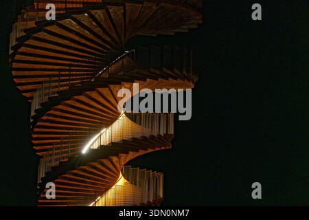 A spiral staircase climbs upward and widens as it rises, silhouetted against a dark sky. The unusual geometry creates a striking architectural shape a Stock Photo