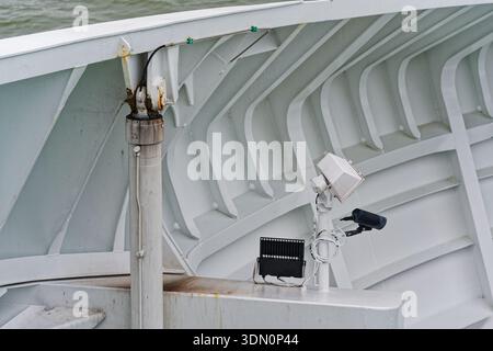 Inside the ship a black camera and a small lamp share one post on the metal wall, aimed along the deck edge, with the sea visible beyond the structure Stock Photo