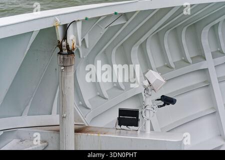 Inside the ship a black camera and a small lamp share one post on the metal wall, aimed along the deck edge, with the sea visible beyond the structure Stock Photo