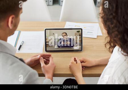 Company employees having online video call with colleague using tablet sitting in office. Stock Photo