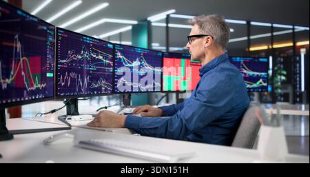 Experienced Trader Analyzing Market Trends On Computer Screens At Exchange. Stock Photo