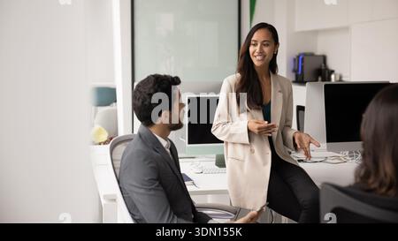 Smiling young woman explaining strategy to diverse team members Stock Photo