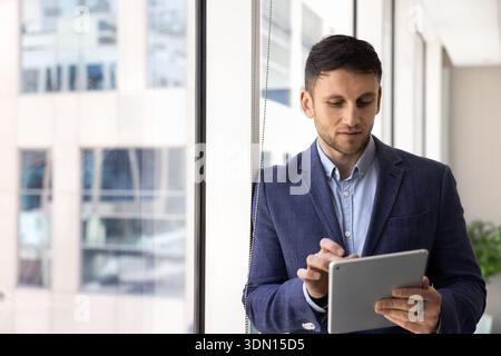 Serious man in suits stands in corporate office with tablet Stock Photo