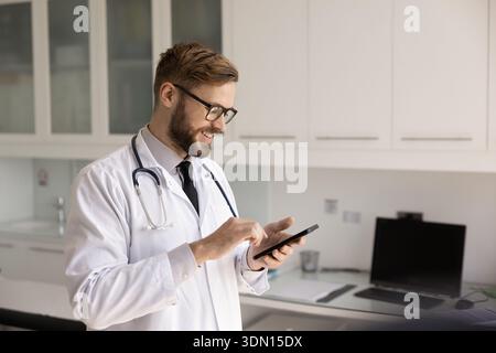 Smiling young male doctor using phone app in hospital office Stock Photo