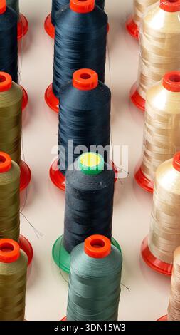 Rows of thread spools in various colors on a flat surface in a crafting area Stock Photo