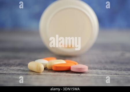Various pills scattered near an open container on a surface Stock Photo