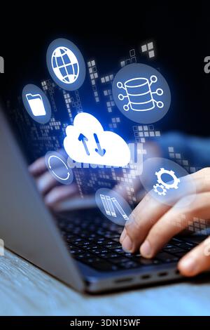 Hands using a laptop with cloud computing icons in a dark setting Stock Photo