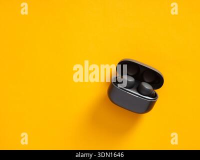 Wireless earbuds charging inside their black case, sitting on a vibrant yellow surface with copy space Stock Photo