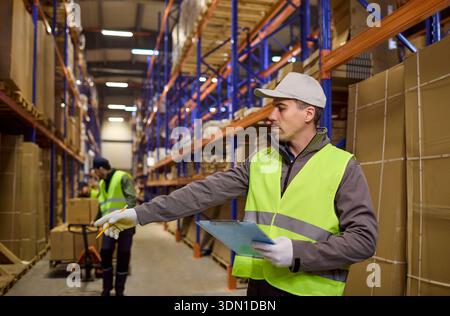 Warehouse logistics worker directing loading while checking inventory on shelves Stock Photo