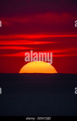 Red sunset over the sea horizon with a dark silhouette of distant hills. Stock Photo