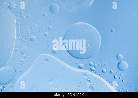 Water and oil droplets mixing on blue surface forming an abstract liquid background Stock Photo