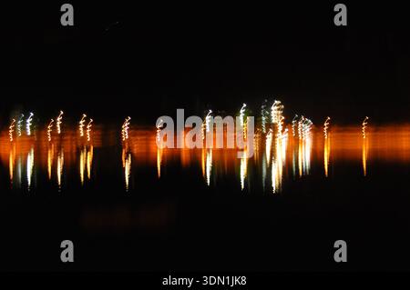 Nighttime city lights shine over a glowing river. Long bridge stretches ...