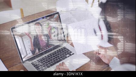 Viewing laptop presenter in blazer gesturing at desk, colleague holding diagram with code overlay Stock Photo