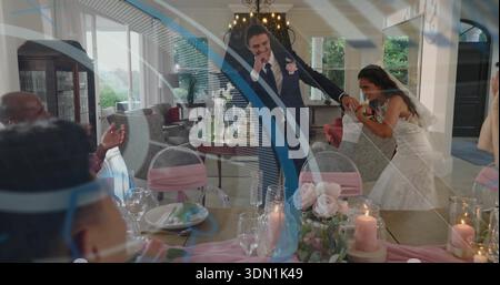 Leaning bride in white gown holding groom's hand in dark suit at home reception, with candles Stock Photo