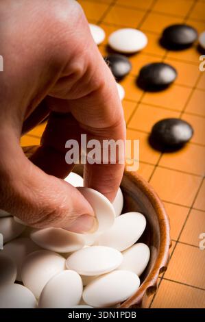 Close-up of a hand placing stones on a Go board, symbolizing strategic thinking, patience, and classic abstract board game play Stock Photo