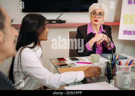 Confident senior businesswoman leading a professional meeting with a diverse team in a modern office environment, discussing strategy, collaboration, Stock Photo