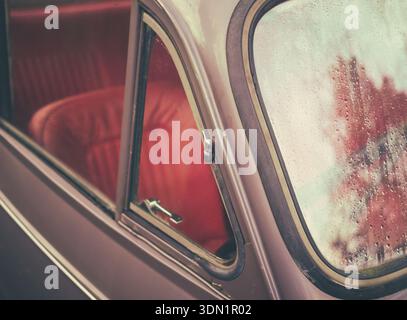 Nostalgic Image Of A Vintage British Car Side Window With Rain Drops On Glass And Red Leather Interior Visible Inside Stock Photo