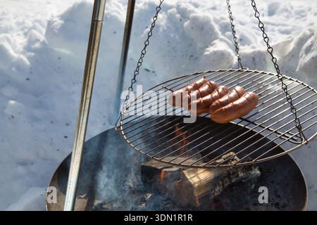 Grilling sausages over an open fire in snowy outdoor setting. Stock Photo