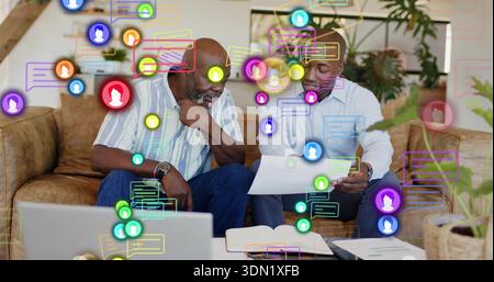 Reviewing paperwork father and son in striped, blue shirts using laptop with chat overlays at home Stock Photo