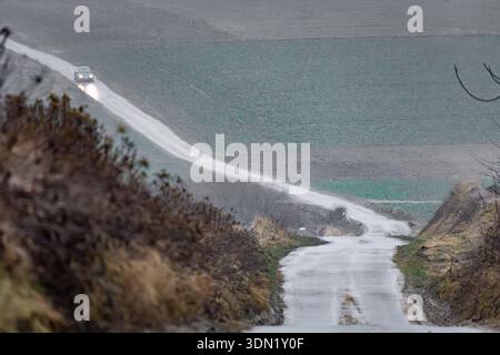Car with headlights driving along foggy rural road through autumn farmland in Central European countryside. Stock Photo
