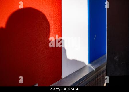 An abstract composition featuring vertical bands of red, white, and blue with a prominent soft shadow cast on the red textured surface. Stock Photo