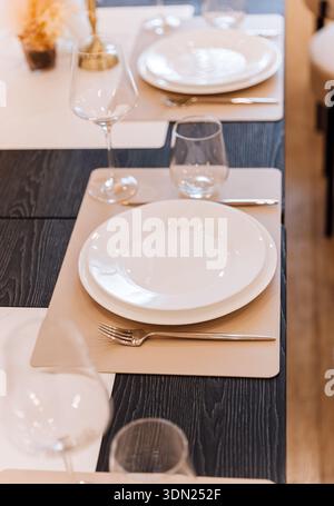 Minimal restaurant place setting with white plate, glassware, beige placemat Stock Photo