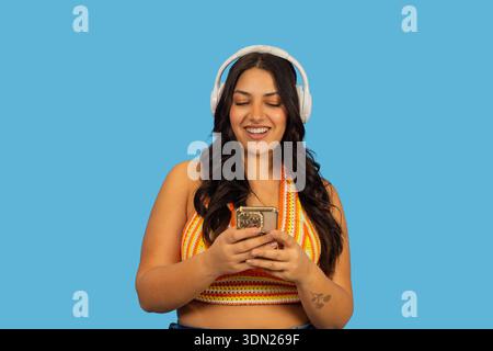 Young woman smiling, using a smartphone and listening to music through headphones Stock Photo