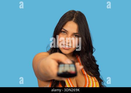 Woman holding a remote control, looking at camera and changing the channel Stock Photo