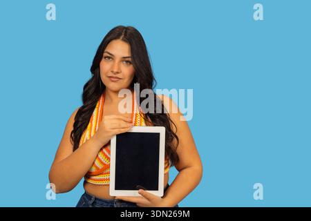 Young woman holding a digital tablet with a blank screen on a blue background Stock Photo