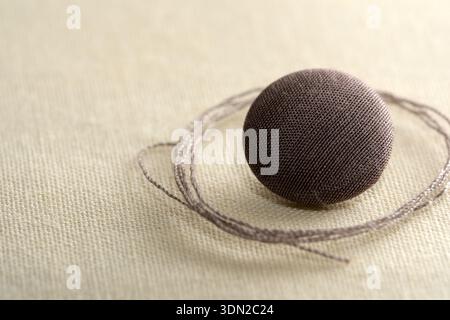A small brown button rests on delicate fabric, with thread elegantly wrapped around it. Stock Photo
